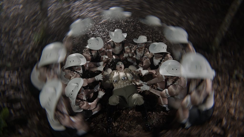 Venice Biennale 2026 — Natasha Tontey, The Phantom Combatants, 2026, video still, postavy v bielych klobúkoch obklopujú postavu na zemi, fisheye objektív.