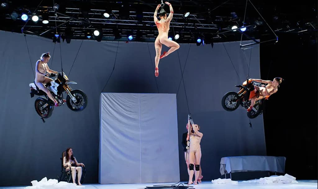 Záber z performancie Florentiny Holzinger TANZ, 2019 — performerky zavesené nad javiskom, dve na motocykloch, jedna vo vzduchu, City of Women, Ľubľana.
