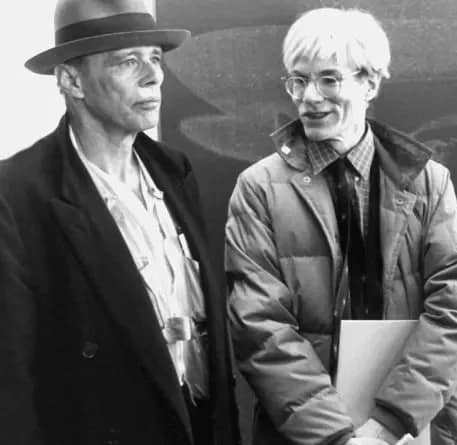 Joseph Beuys v klobúku a Andy Warhol v páperovej bunde, fotografovaní spolu v roku 1982. V pozadí čiastočne viditeľný Warholov portrét.