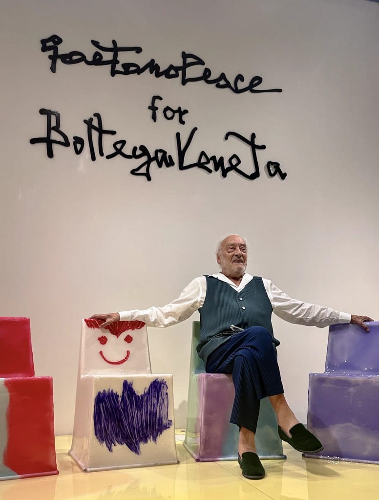 Gaetano Pesce sedí medzi farebnými plastovými stoličkami s detskými kresbami v priestore Bottega Veneta.